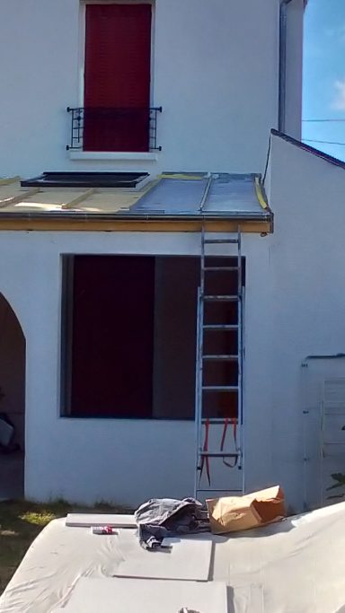 Échelle appuyée contre un bâtiment en cours de rénovation, avec un toit partiellement refait.