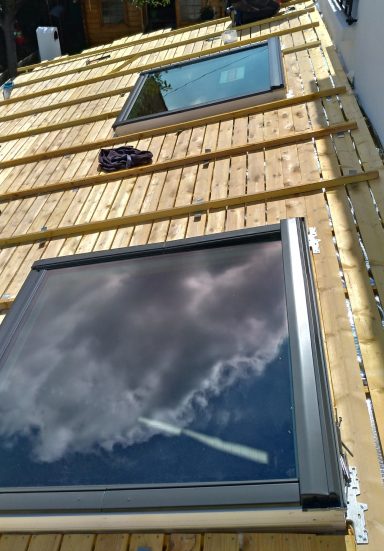 Fenêtres de toit reflétant des nuages, sur une structure en bois.