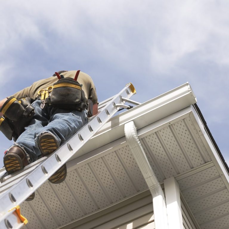 Un homme grimpe sur une échelle pour travailler sur le toit d'une maison.