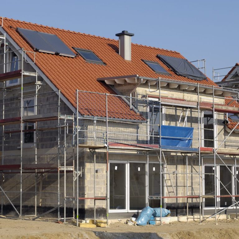 Maison en construction avec échafaudages et panneaux solaires sur le toit.