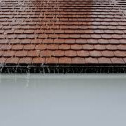 Gouttes de pluie tombant sur un toit en tuiles, avec un plan d'eau en dessous.