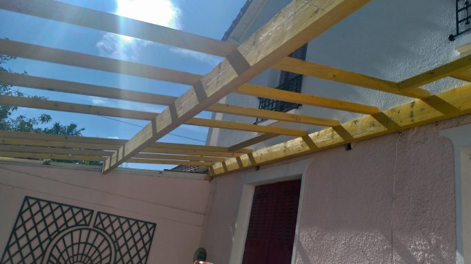 Structure en bois aux poutres jaunes, partiellement recouverte, ciel bleu en arrière-plan.
